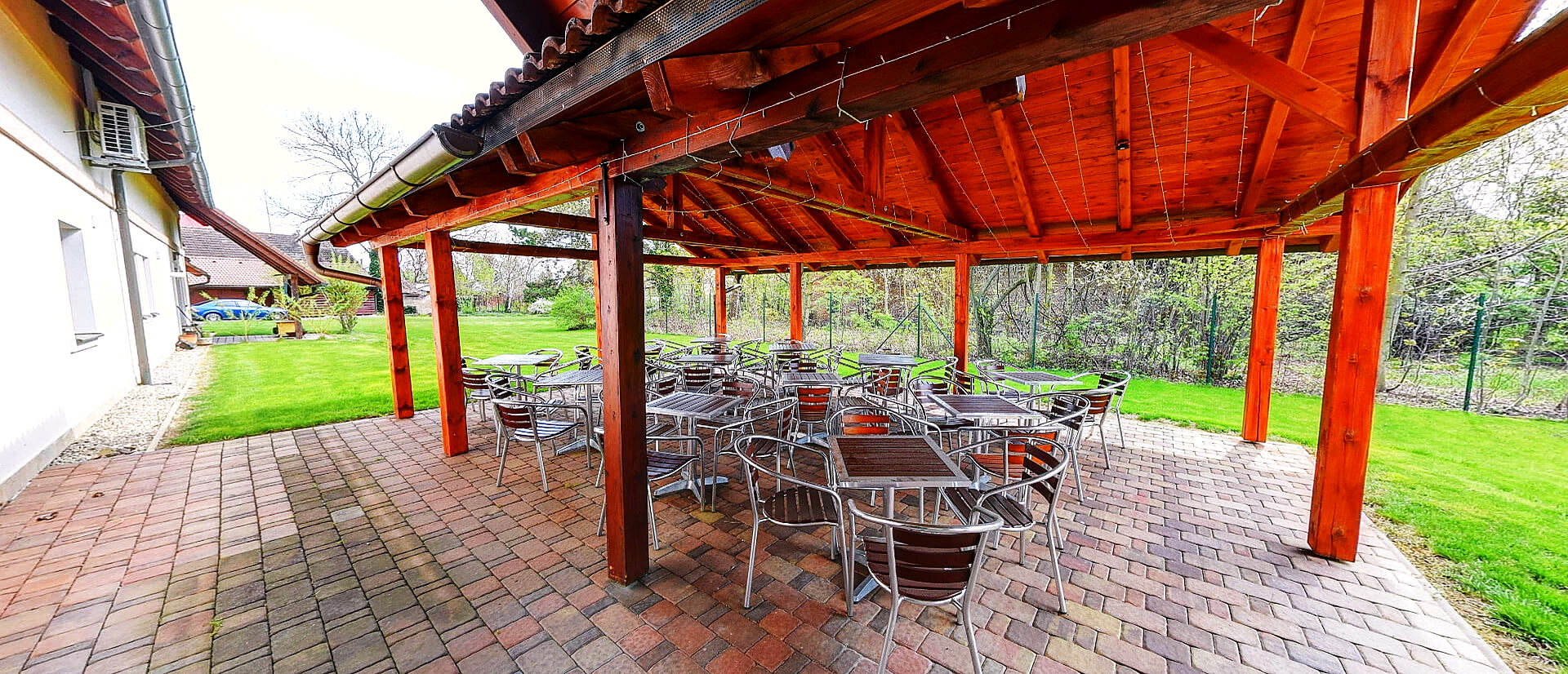 Krytá pergola se stoly v zahradě penzionu — prostor pro grilování